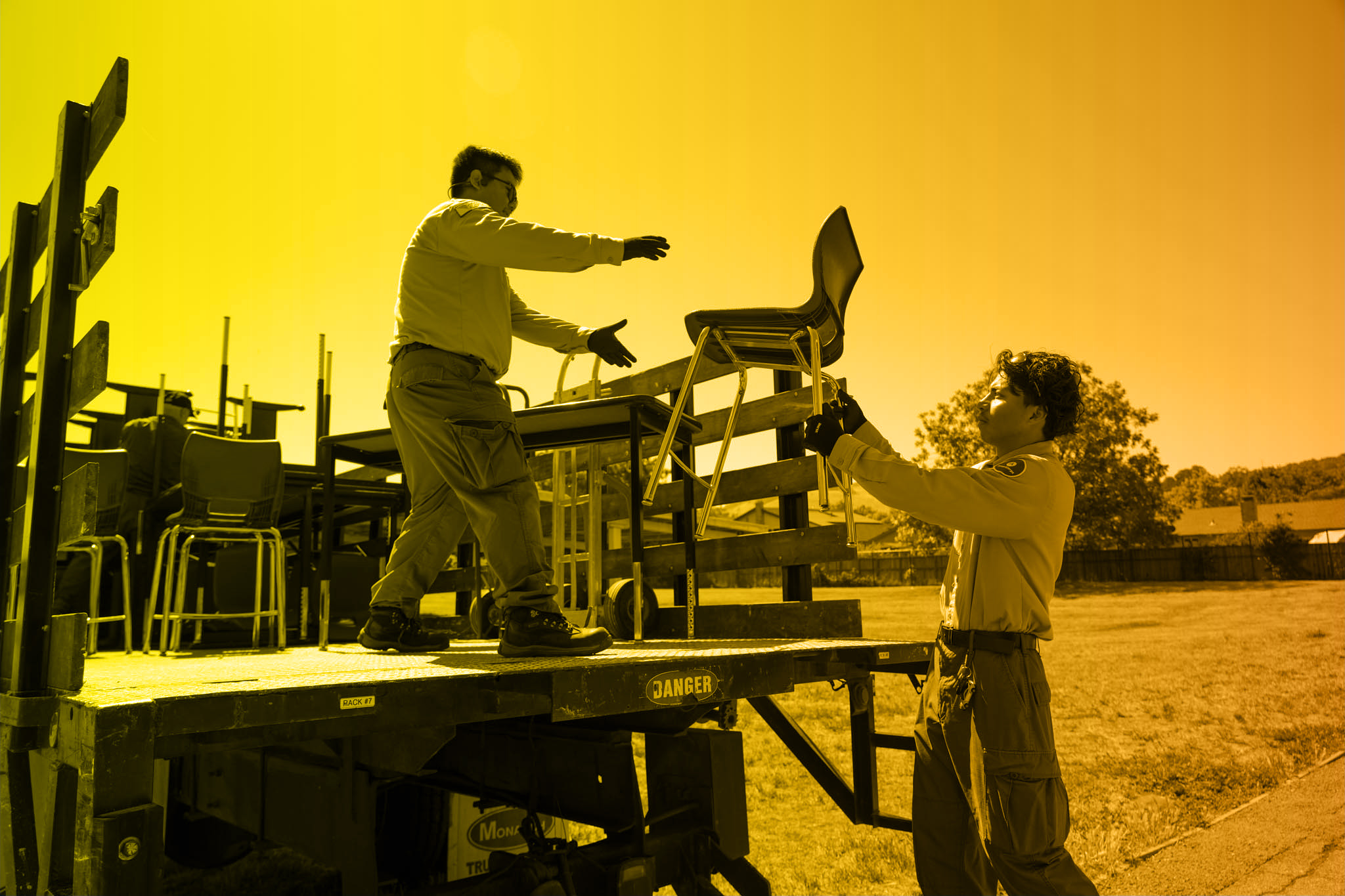 Corp members loading chairs onto truck – Two corp members work together to load blue classroom chairs onto the back of a flatbed truck.