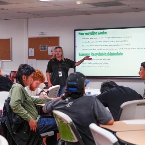 Recycling education session – A staff instructor leads a recycling training session in front of a classroom, with a slide presentation on how recycling works displayed on a screen.