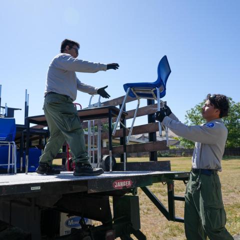 Corp members collecting reusable furniture – Two corp members load blue school chairs onto a flatbed truck as part of a furniture reuse or recycling program.