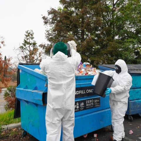 Corp members sorting landfill waste – Corp members wearing full protective suits sort trash from blue dumpsters labeled “Landfill Only” during a waste audit.